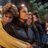 A young person in a yellow coat embraces a woman wearing a black jacket from behind.