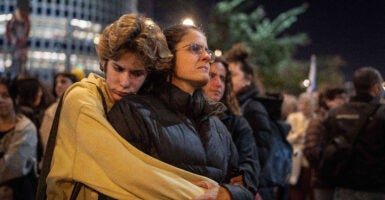 A young person in a yellow coat embraces a woman wearing a black jacket from behind.