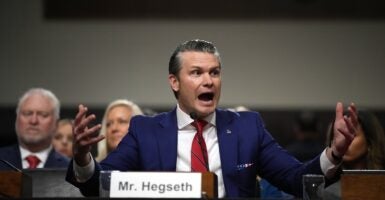 Pete Hegseth raises his arms and talks in an animated fashion during a Senate hearing