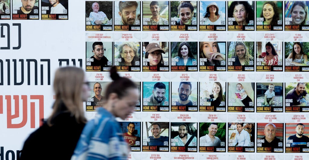 Women in Israel pass by a wall covered with photos of hostages being held by Hamas