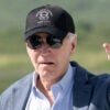 Joe Biden in a blue shirt and a grey sport coat waves in a hat reading "Presidential Retreat Camp David"