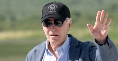 Joe Biden in a blue shirt and a grey sport coat waves in a hat reading 