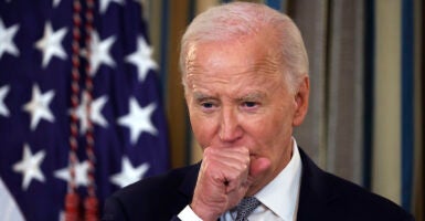 Joe Biden in a black suit puts his hand in front of his mouth