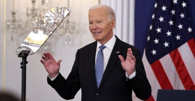 Joe Biden in a black suit with a blue tie and American flag pin raises his hands