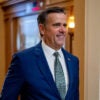 John Ratcliffe smiles while walking in a blue suit