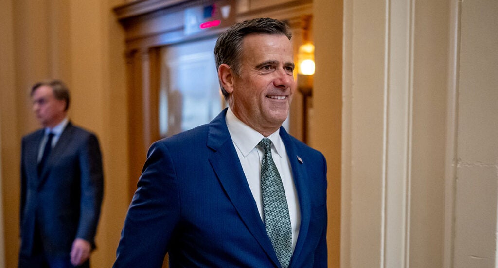 John Ratcliffe smiles while walking in a blue suit