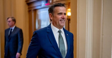 John Ratcliffe smiles while walking in a blue suit