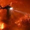 A helicopter flies above a raging fire and drops water.