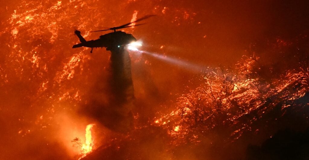 A helicopter flies above a raging fire and drops water.