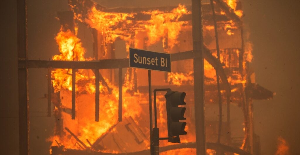 A Sunset Boulevard street sign hangs near a traffic light as a raging fire goes on behind.