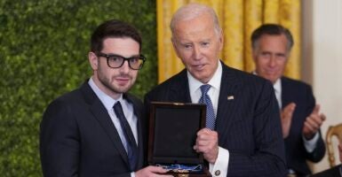 Alex Soros and Joe Biden both hold the Medal of Freedom while they pose for a photo.