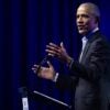 Barack Obama stands at a podium talking with his arms wide open.