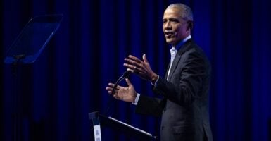 Barack Obama stands at a podium talking with his arms wide open.