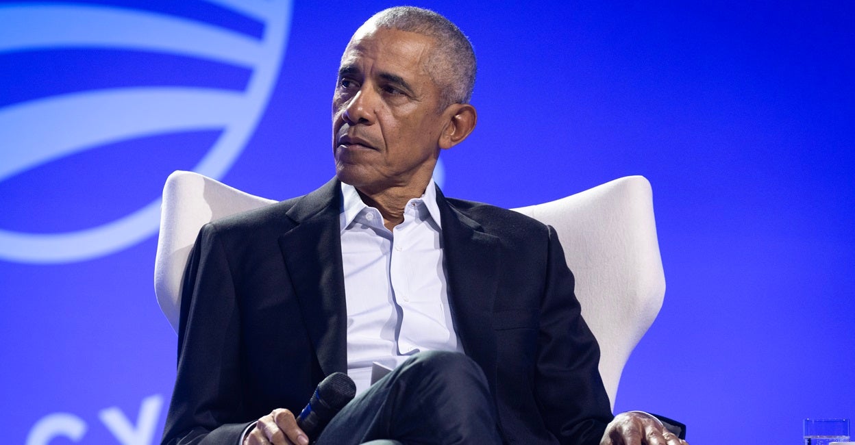 Former President Barack Obama sits in a chair holding a microphone.