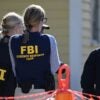 Government agents wearing vests with FBI written on them stand at a crime scene.