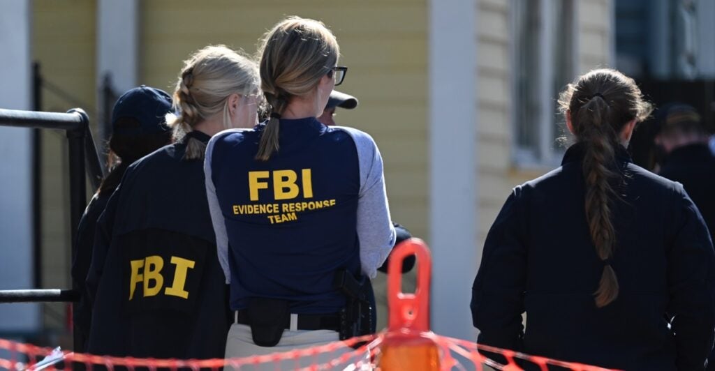 Government agents wearing vests with FBI written on them stand at a crime scene.