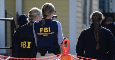 Government agents wearing vests with FBI written on them stand at a crime scene.