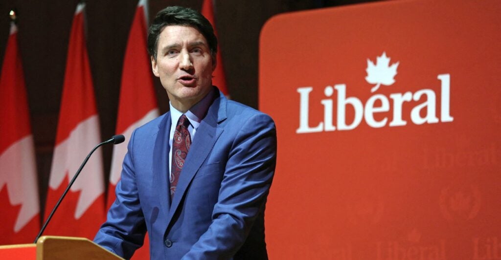 Justin Trudeau stands at a podium next to a banner that says, "Liberal".