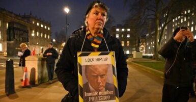 A Donald Trump protest wearing winter clothing holds a placard of Trump with an image of his mug shot.