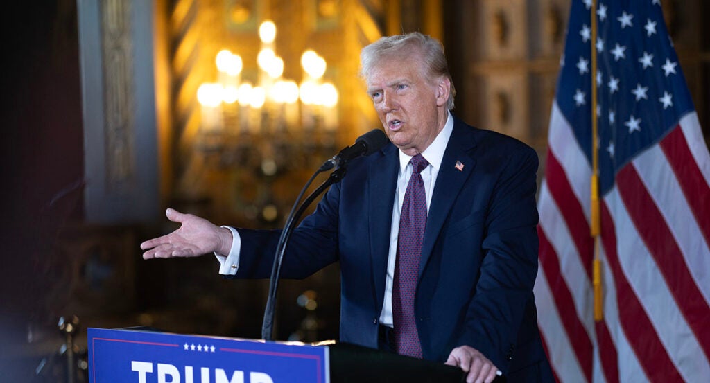 Donald Trump gestures in a suit in front of an American flag