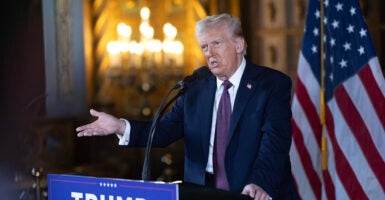 Donald Trump gestures in a suit in front of an American flag