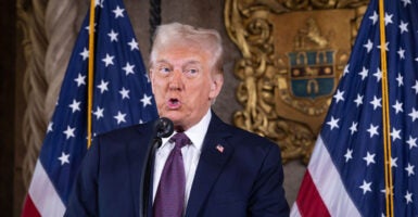 Donald Trump in a blue suit speaks in front of an American flag