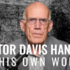 Victor Davis Hanson in a gray suit jacket with a microphone looking directly at the camera