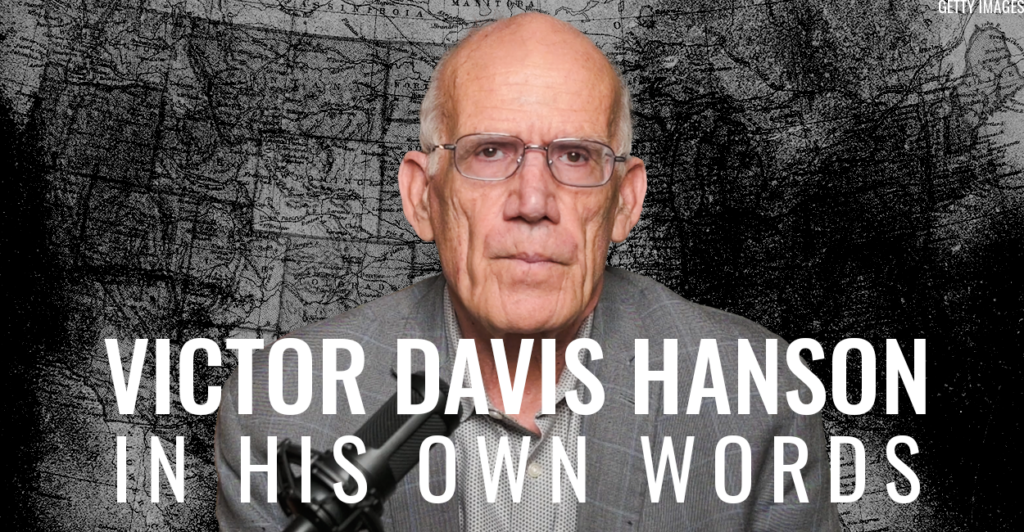 Victor Davis Hanson in a gray suit jacket with a microphone looking directly at the camera