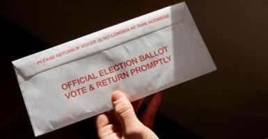 A hand holds an absentee ballot in a mail-back envelope.