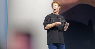 Facebook founder Mark Zuckerberg stands on a stage and talks to someone in the audience.