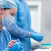 a female medical professional in blue scrubs and a mask comforts a woman lying on a surgical table in an operating room