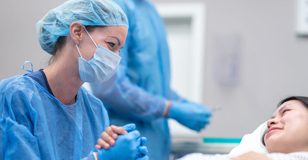 a female medical professional in blue scrubs and a mask comforts a woman lying on a surgical table in an operating room