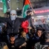 Crowds of Gazan men celebrate in the streets, raising one man holding two Palestinian flags in the air.