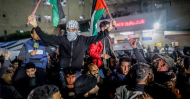 Crowds of Gazan men celebrate in the streets, raising one man holding two Palestinian flags in the air.