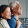 An older black couple is hugging in the kitchen.