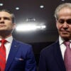 Pete Hegseth in a blue suit and red tie stands alongside former Senator Norm Coleman in a dark suit in a Senate committee hearing room