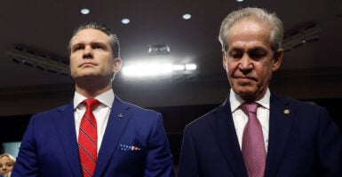 Pete Hegseth in a blue suit and red tie stands alongside former Senator Norm Coleman in a dark suit in a Senate committee hearing room