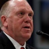 Tom Homan speaks into a microphone while seated and wearing a dark suit and red tie.