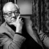 Jean-Marie Le Pen poses for a photo In a sport coat, seated with his chin resting his hand