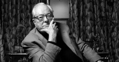 Jean-Marie Le Pen poses for a photo In a sport coat, seated with his chin resting his hand