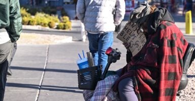 A homeless man sits on a sidewalk holding up a sign.