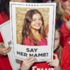 Trump supporters in red Trump 2024 T-shirts hold up signs of a photo of a slain Laken Riley with the caption "say her name!"