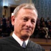 Chief Justice of the United States John Roberts Standing on the floor of the House of Representatives in a tie and black judicial robe with people filling gallery balcony behind him