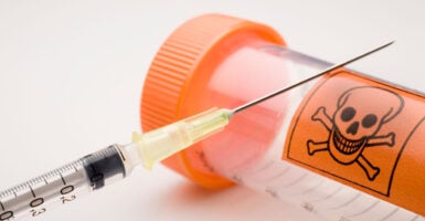 A picture of a hypodermic needle leaning against a vial with a skull and crossbones on it