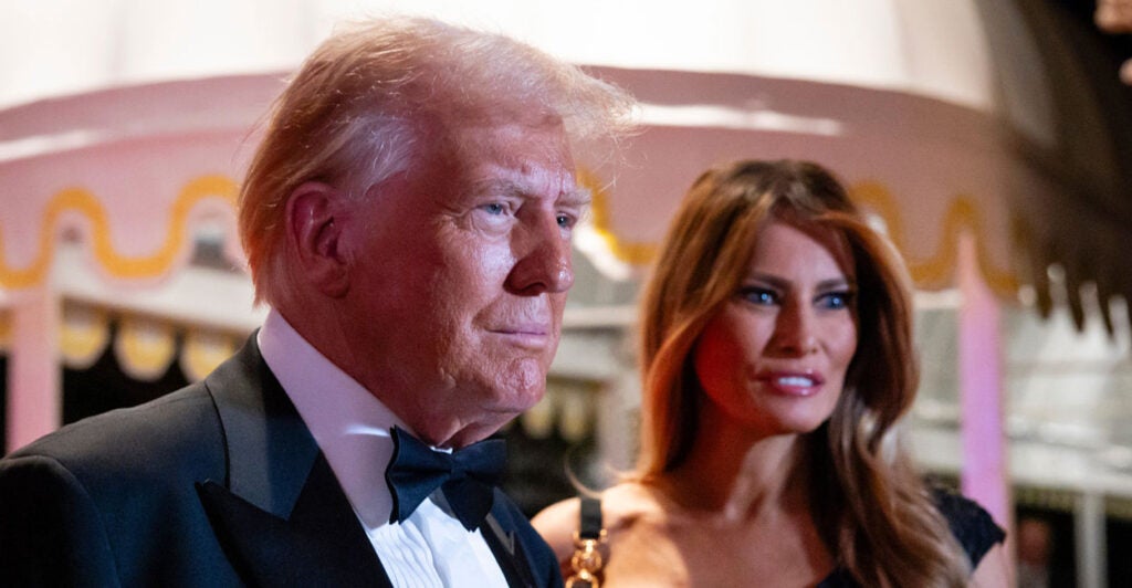 President Donald Trump in a tuxedo stands next to his wife Melania in a black dress at an event.