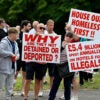 Several British men on a roadside protesting illegal aliens with large signs that say things such as "stop the boats"