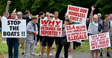 Several British men on a roadside protesting illegal aliens with large signs that say things such as 