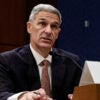 Ken Cuccinelli in a dark suit and sitting at a table testifying to a congressional committee