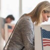 a blonde woman in a white outfit voting at a voting station with an American flag on the side of it