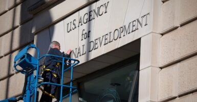 A worker on a platform removes the lettering of the sign on a building.